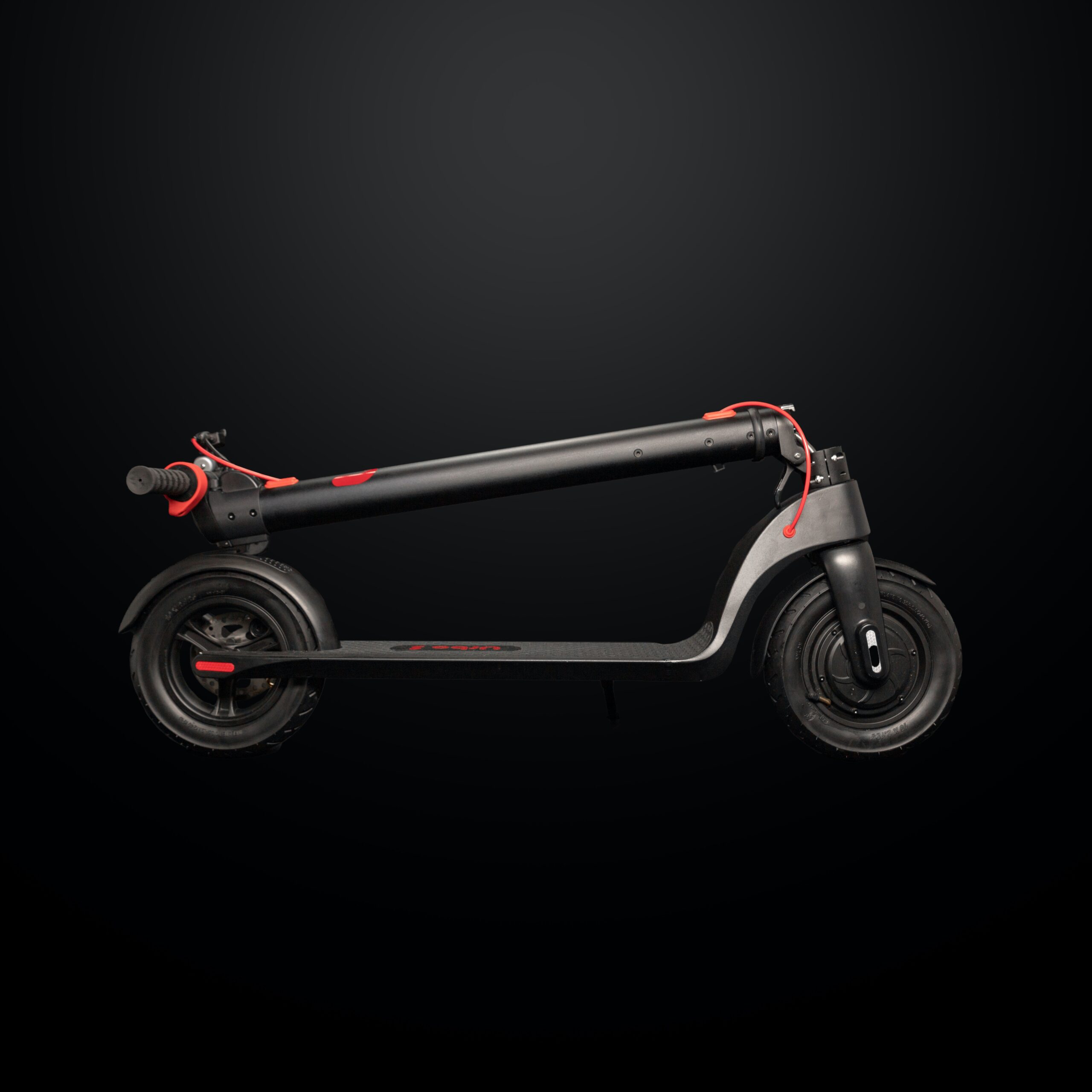 A folded black and red scooter in front of a black backdrop.